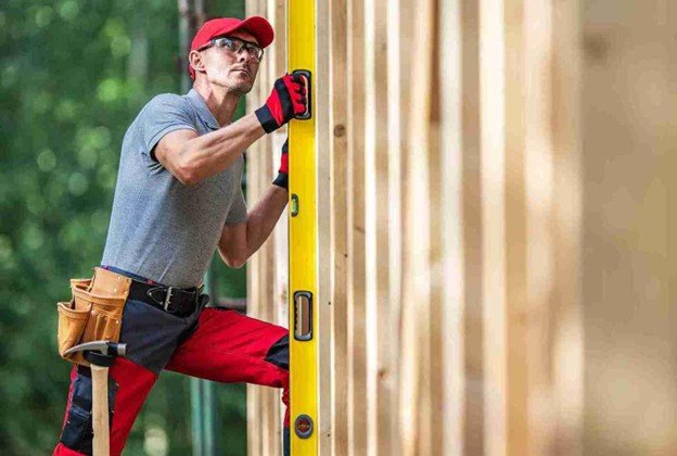 Fence contractor using a level to align wooden posts during cedar fence installation