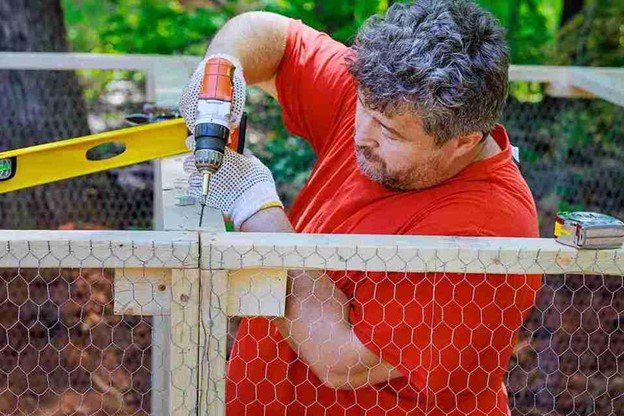 Worker installing a cedar wood fence with a power drill in a sunny residential yard