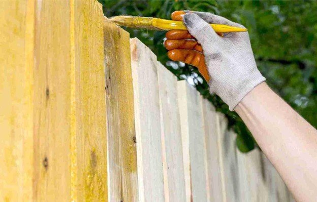 Worker using a brush to apply stain or sealant to a wooden fence board