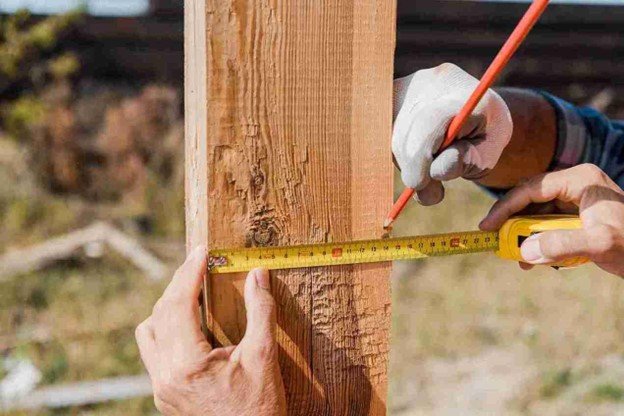 Worker measuring and marking a wooden fence post for accurate installation.
