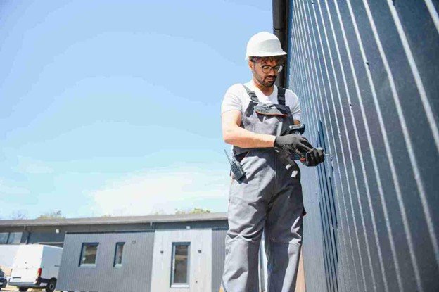 Technician wearing safety gear installing or adjusting a modern metal gate on a commercial building