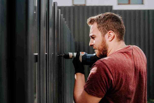 Technician using a power drill to repair or install a modern metal gate
