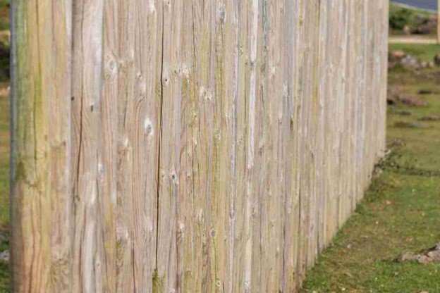 Contractor adjusting a leaning wooden fence along a grassy property line