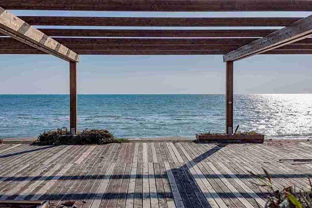 Wooden pergola under construction overlooking the ocean with sunlight reflecting on the water.